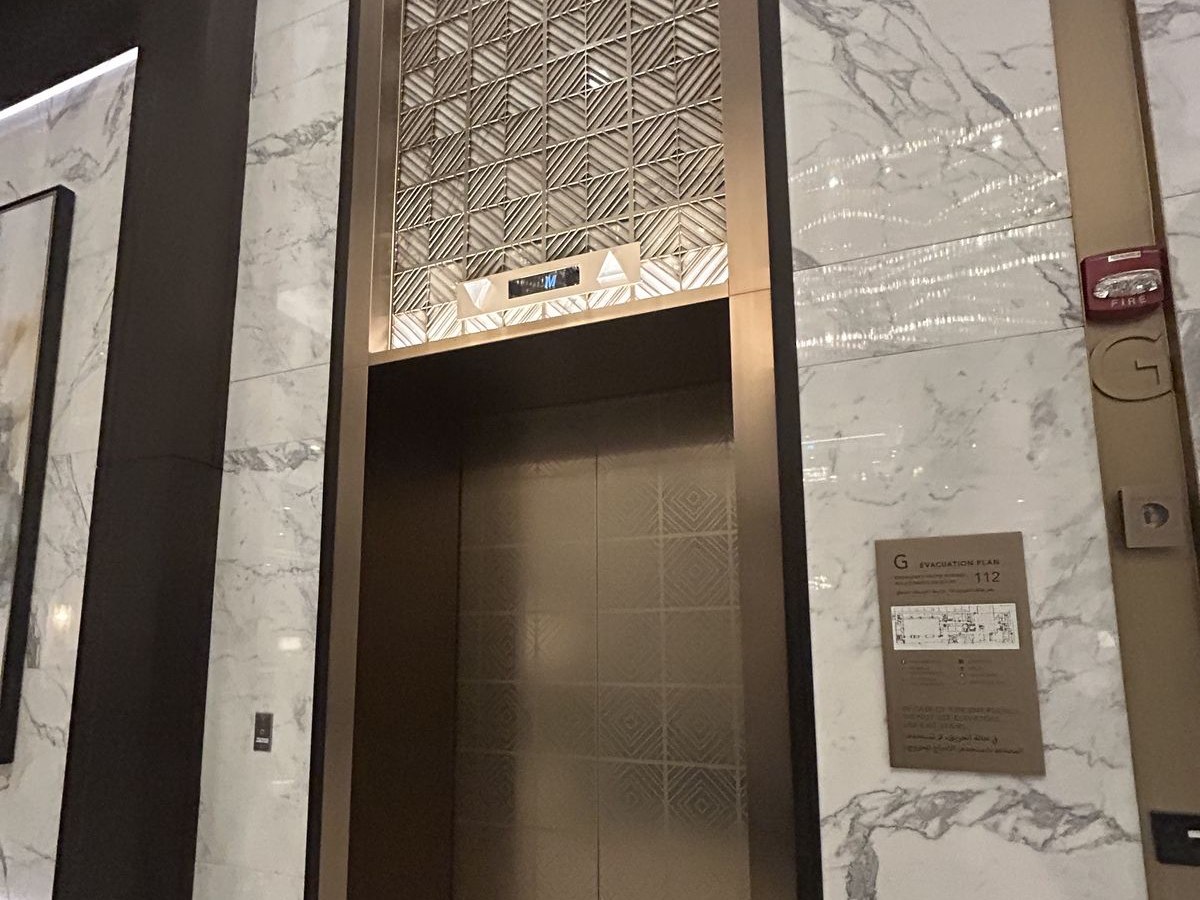 An elevator lobby where a patterned stainless door and surround sit within a marble portal