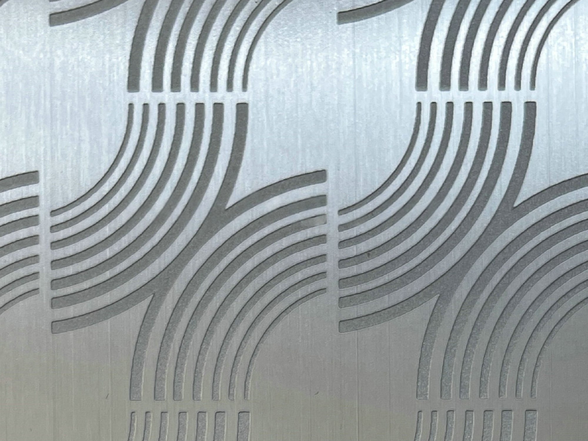 Etched graphic arcs and lines on brushed stainless steel, the etched areas reading matte against the brighter ground