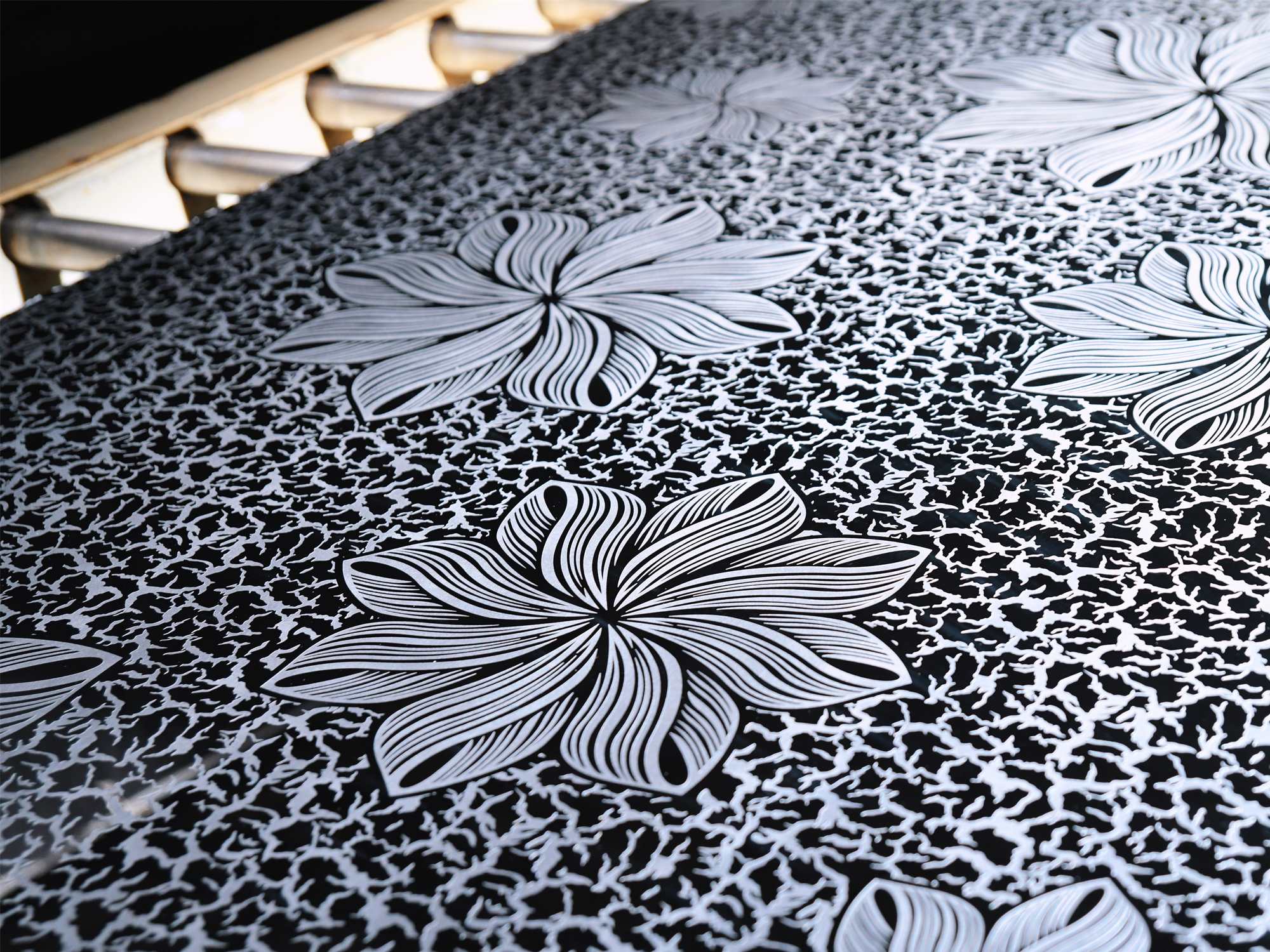 A black mirror stainless steel sheet with an etched floral pattern on the etching line, the etched areas reading matte against the polished ground