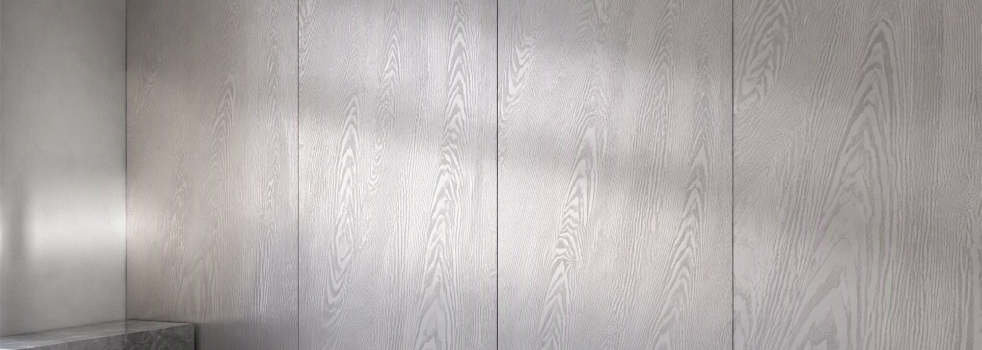 A silver-grey wood-effect printed stainless steel wall in a completed interior, the pattern carried across the full wall plane