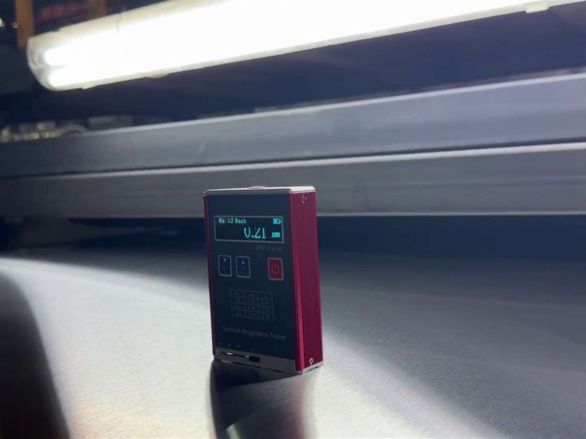 A surface roughness tester resting on a brushed stainless steel sheet, verifying the etched surface in metal rather than on screen