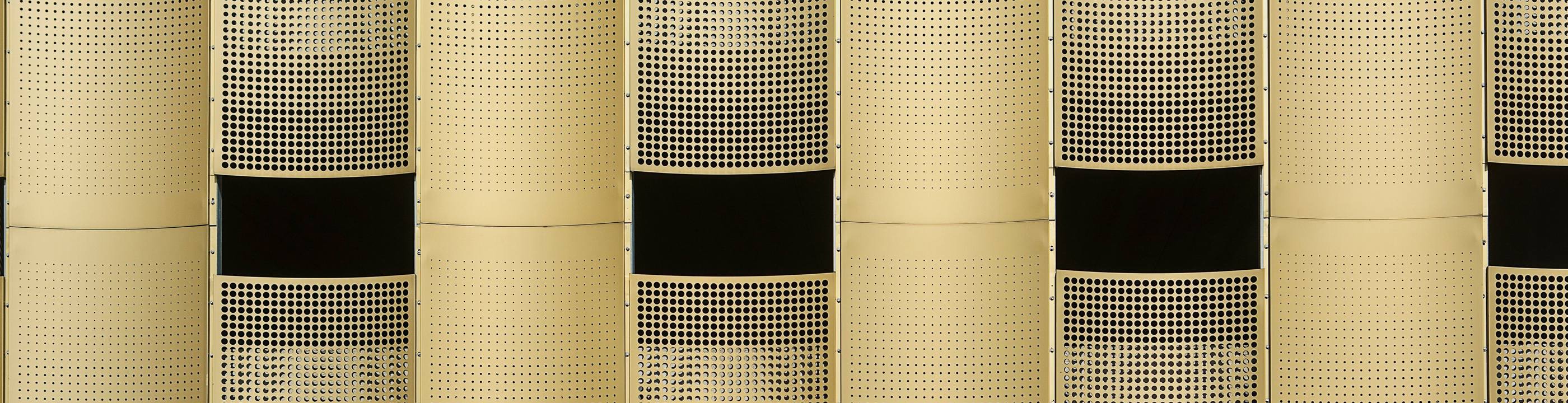 A gold perforated stainless steel facade of perforated panels with recessed dark window bands, controlling light and visibility across the elevation