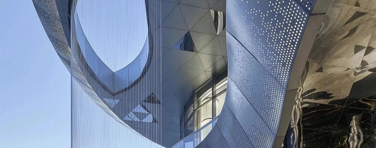 Backlit perforated stainless steel soffit glowing after dark, light passing through the openings to make the pattern luminous