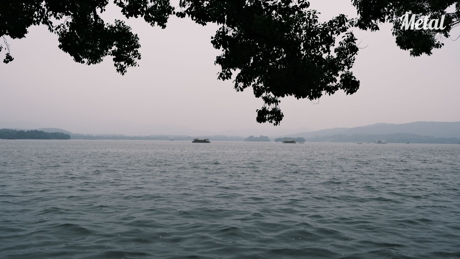 West Lake in Hangzhou under a grey evening sky, with distant hills and small boats