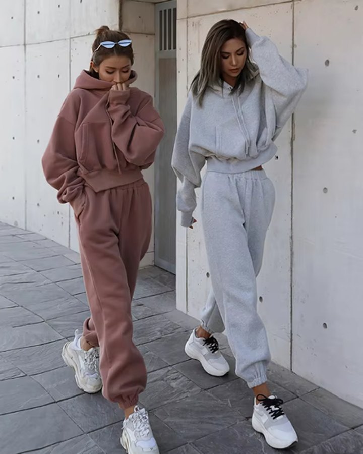 Two models wearing dusty rose and light grey women's hoodie and jogger sets styled as casual tracksuits