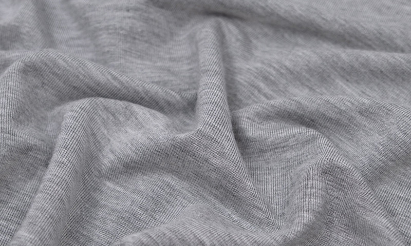Close-up of a soft grey modal knit fabric showing the fluid drape and fine rib texture