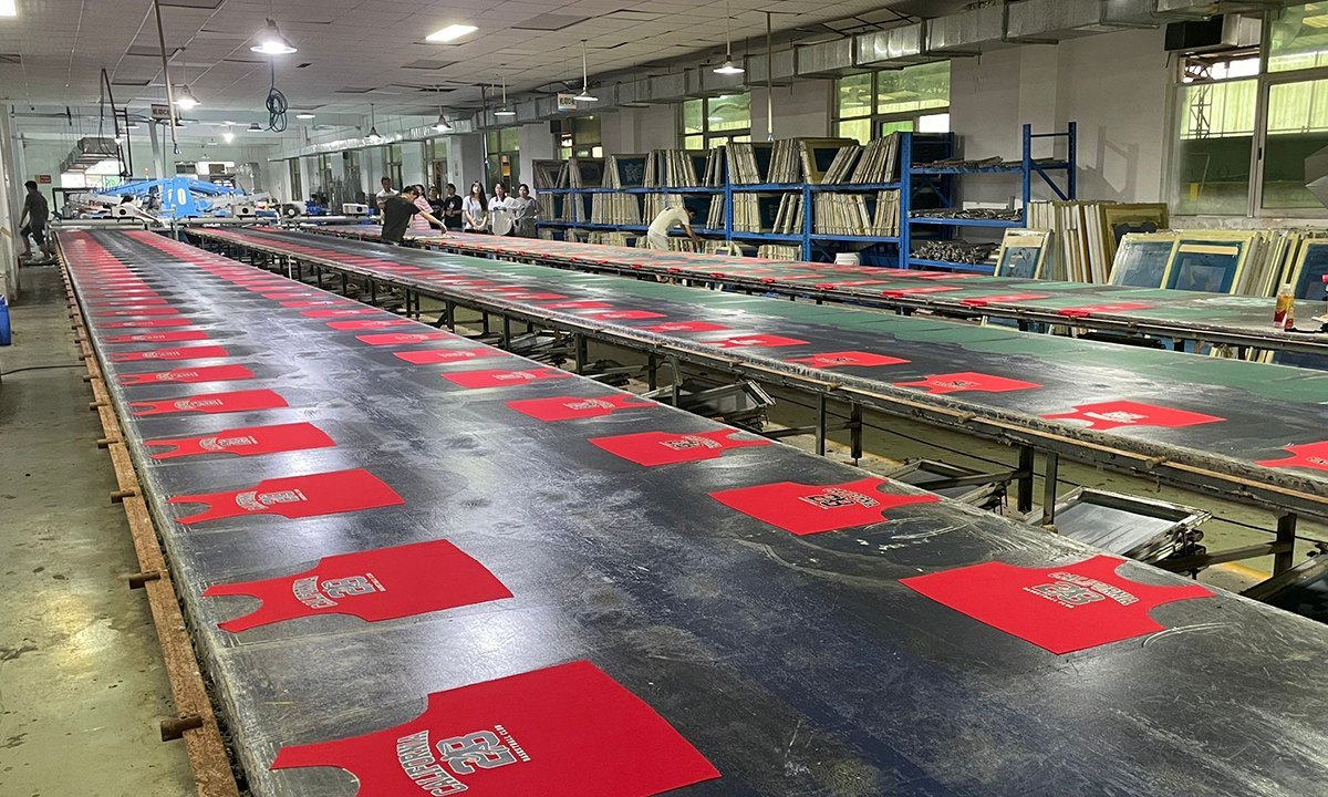 Long screen printing tables with red garment panels drying in a pajama printing factory
