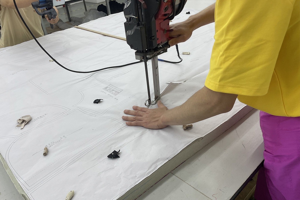 Worker guiding a straight knife cutting machine through many layers of fabric spread on a cutting table