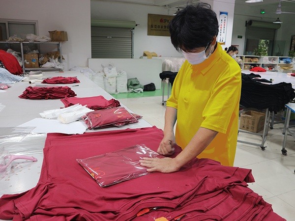 Worker folding and bagging finished garments into clear polybags on a packing table