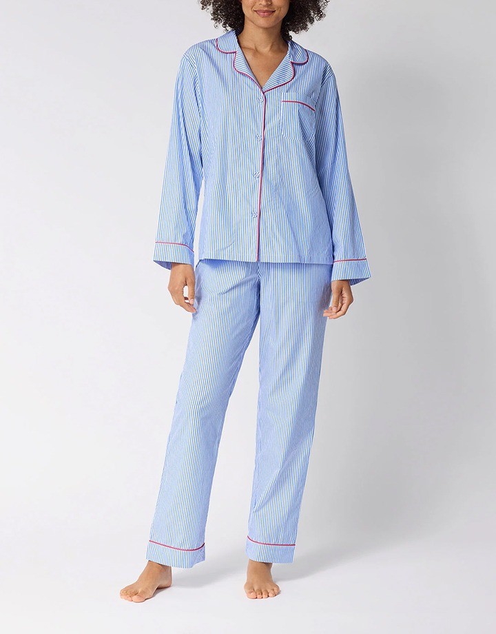 Woman wearing a blue and white striped pajama set with red piping on the collar, cuffs and trouser hems