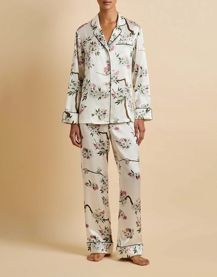 Woman wearing an ivory satin pajama set printed with pink and white blossom branches and black piping