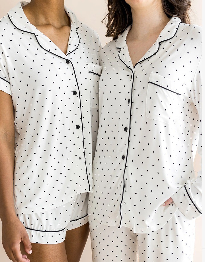 Two women in white polka dot pajamas with black piping, one a shorts set and one a long-sleeve set