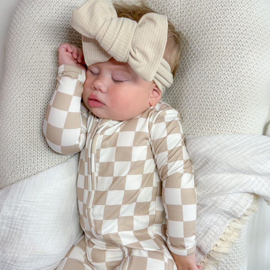 Baby in a beige and white checkered zip sleepsuit on a knitted blanket