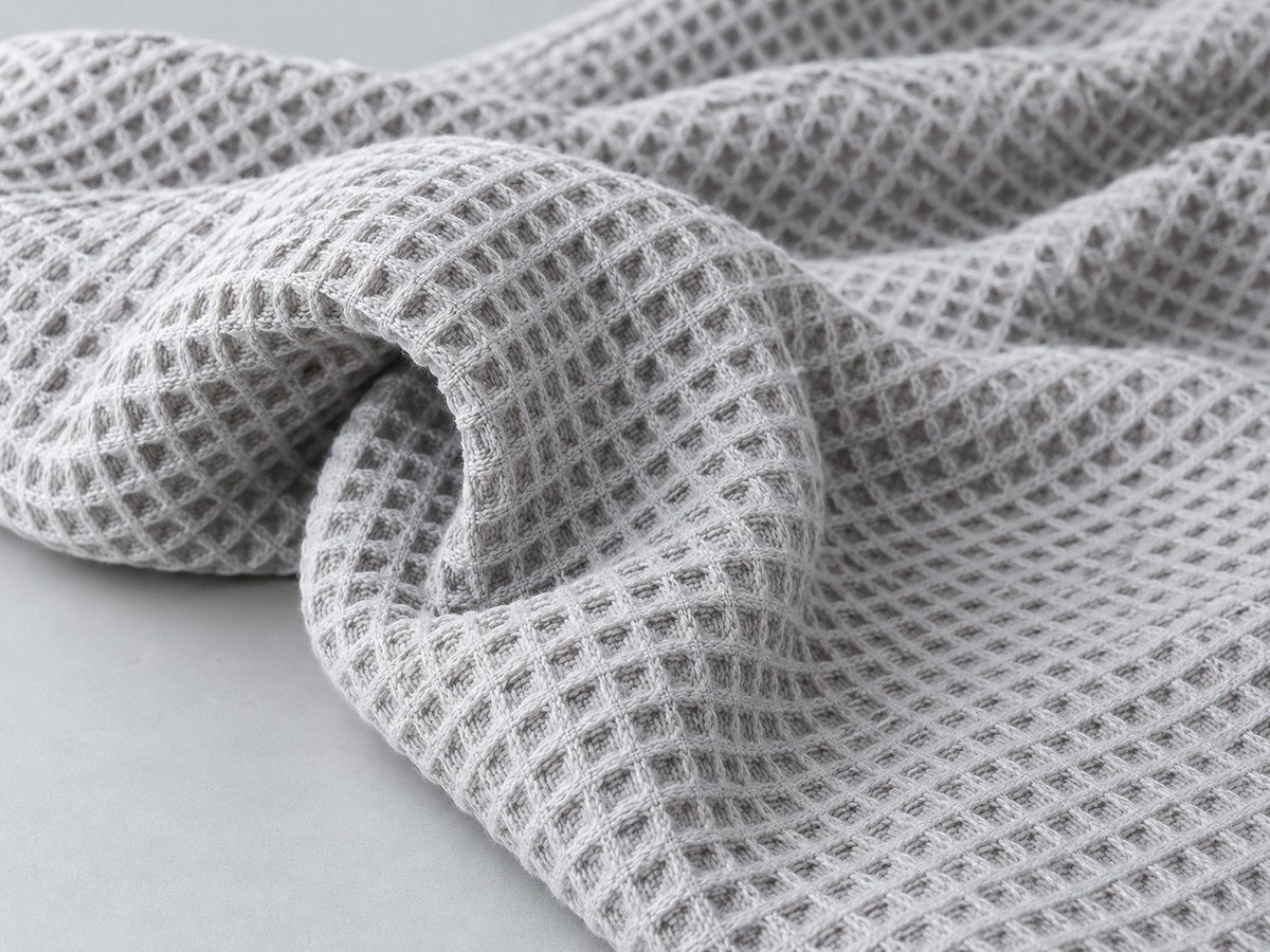 Close-up of light grey cotton waffle fabric showing its recessed honeycomb texture in soft folds
