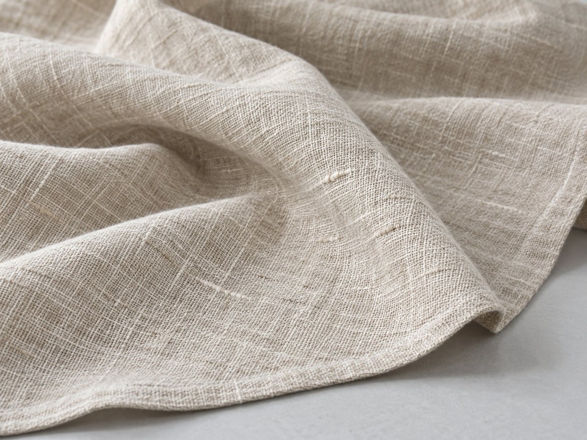 Close-up of natural light linen fabric with visible yarn texture and soft relaxed creases