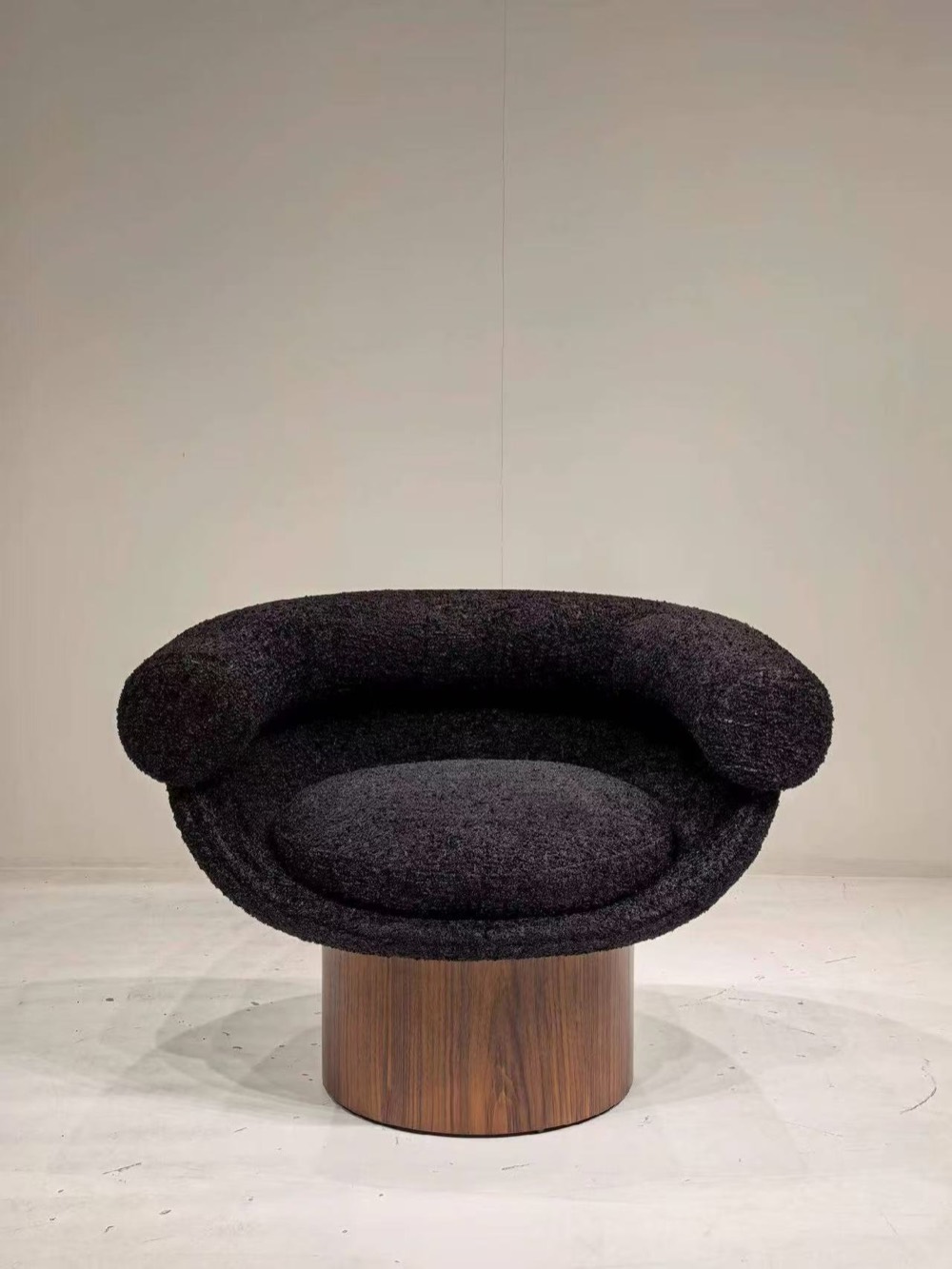 Front view of a black textured lounge chair on a walnut pedestal base