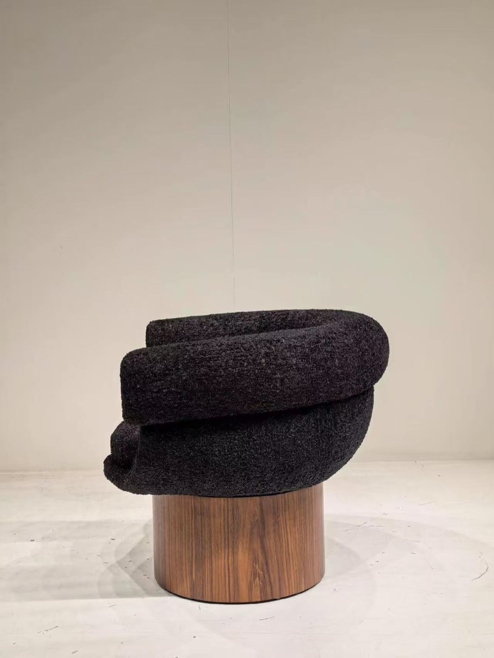 Rear view of black textured lounge chair with walnut pedestal base