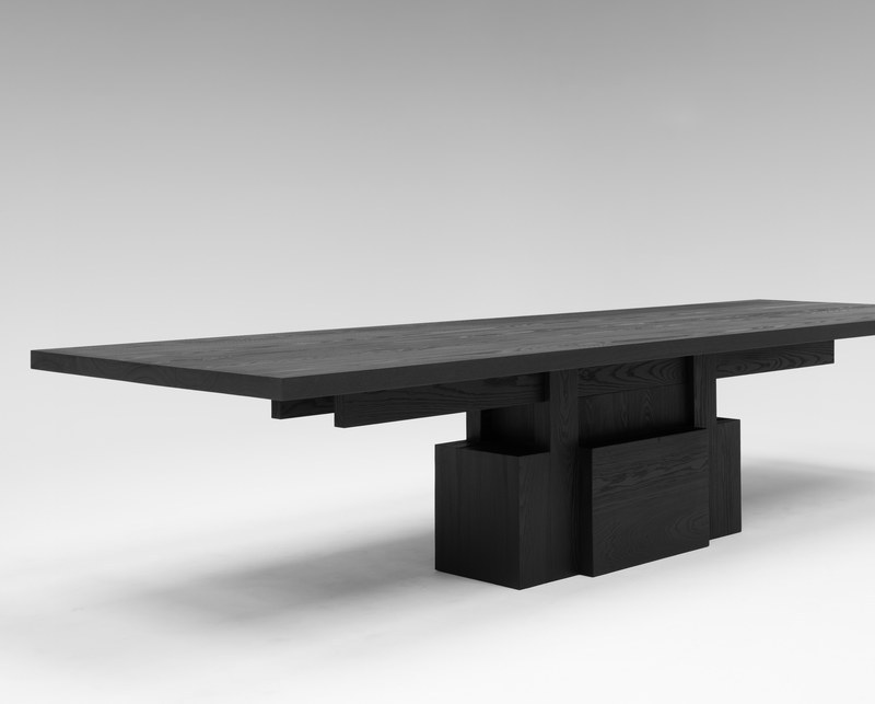 Black wood dining table showing its layered geometric block base and wood grain