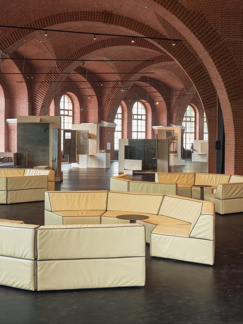 Faceted modular lobby sofas arranged around small round pedestal tables in a brick-vaulted hall