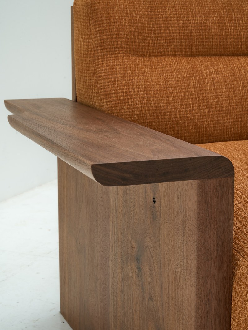 Close-up of a sculpted wooden sofa arm beside textured burnt-orange hotel upholstery