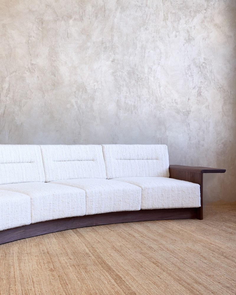 Long front view of an ivory curved hotel sofa showing the continuous seat and low curved wood plinth