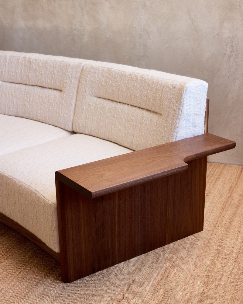 Close-up of a sculptural wood sofa arm beside channel-detailed ivory back cushions