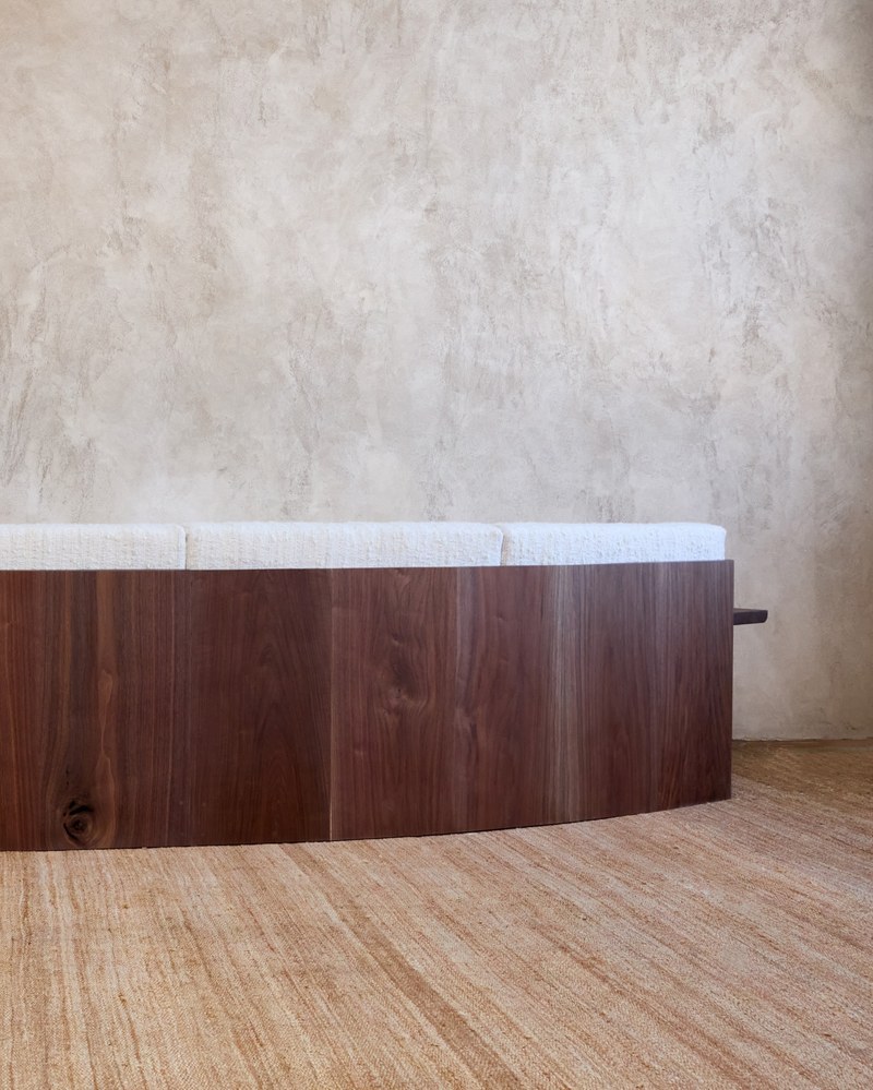 Continuous curved wood back shell of a hotel suite sofa in deep walnut-tone finish