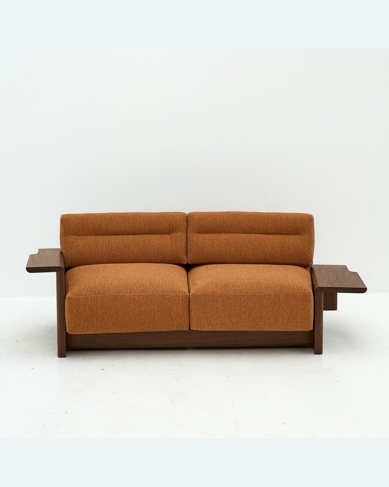 Front view of a custom two-seater hotel sofa with burnt-orange upholstery and sculpted wood arms