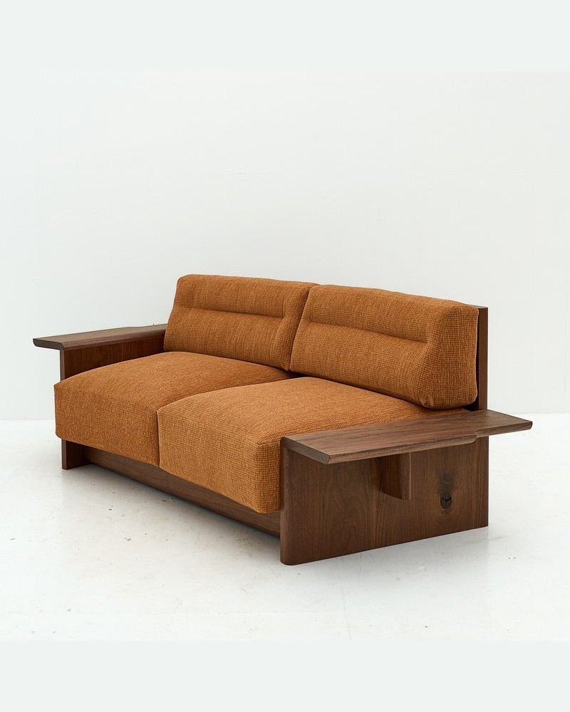 Angled view of a burnt-orange hotel sofa showing the textured woven fabric and dark wood side panel