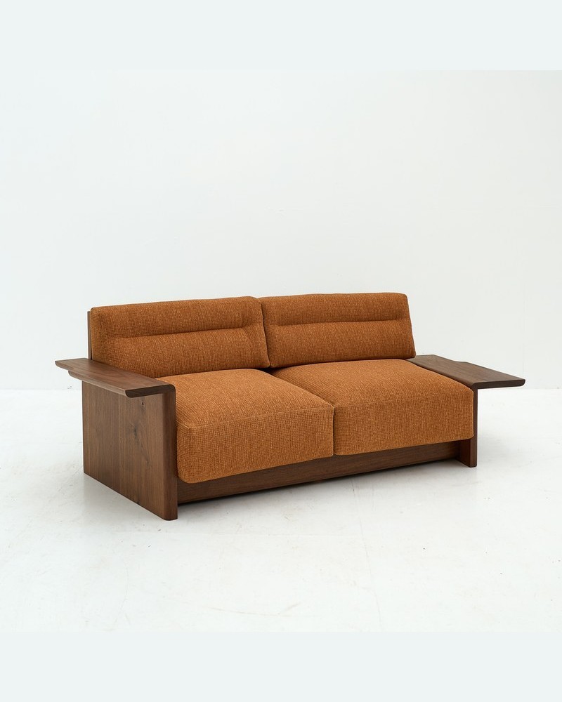 Three-quarter view of a custom hotel sofa with exposed wood frame and low-profile base