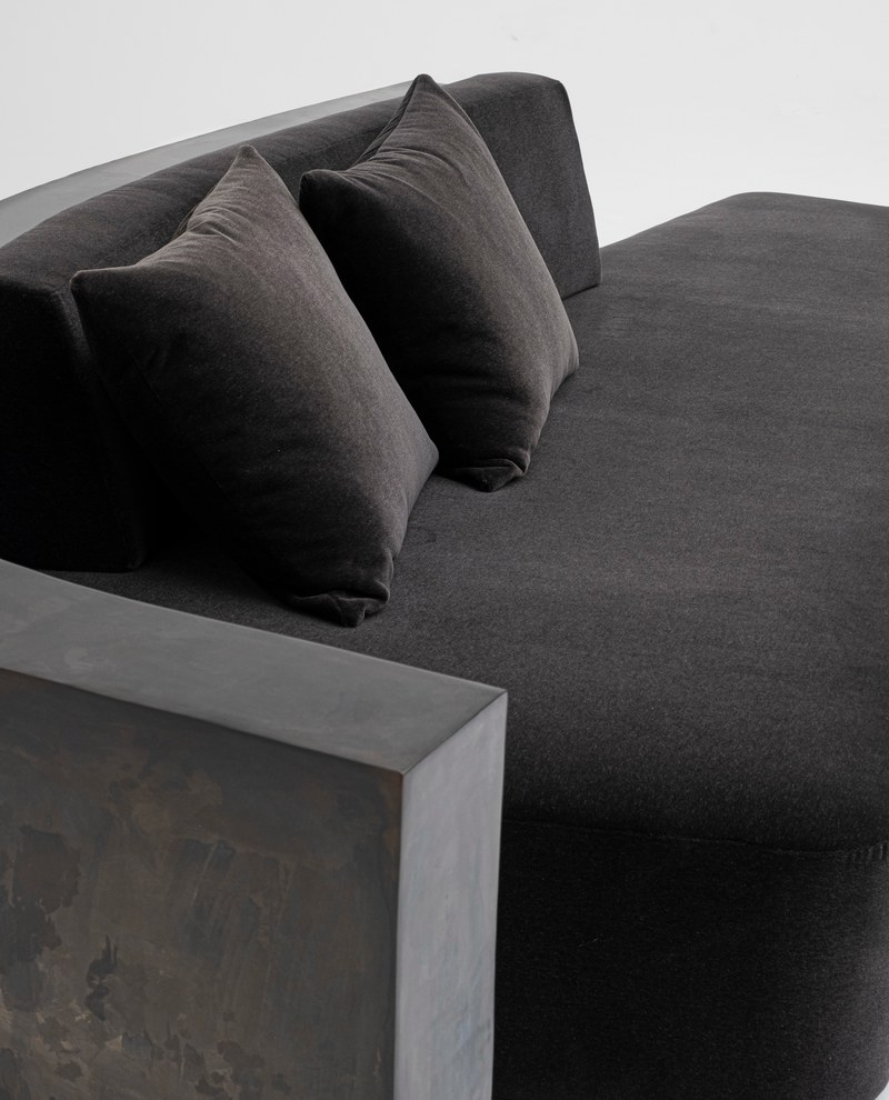 Close-up of a charcoal upholstered chaise seat with two cushions and dark stone surround