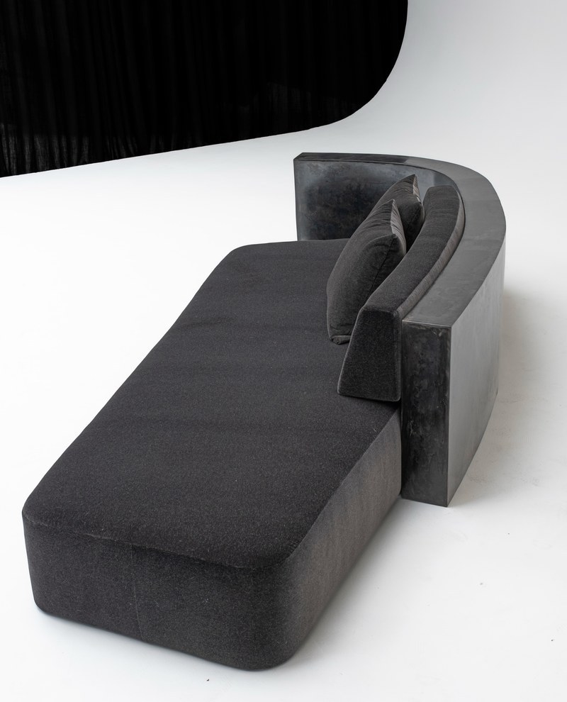 Three-quarter view of sculptural dark marble surround and low-profile upholstered chaise lounge