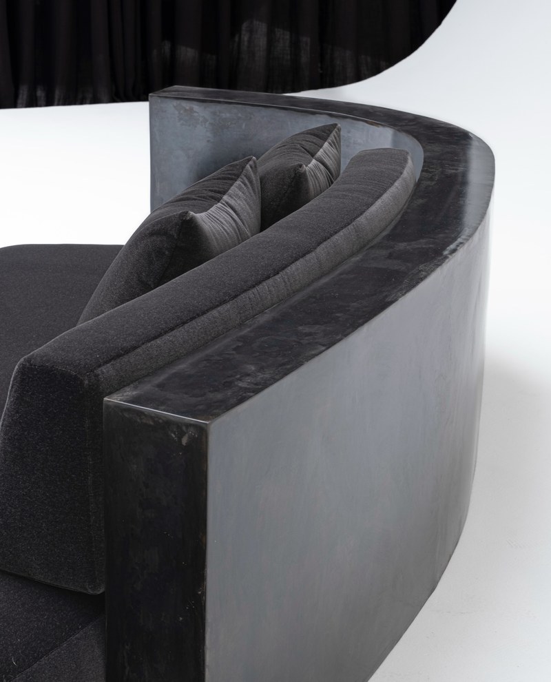 Rear detail of a dark mottled curved surround framing a charcoal upholstered chaise