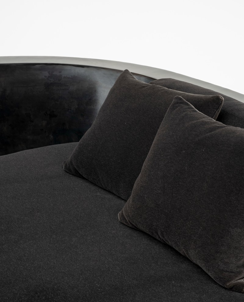 Close-up of two charcoal throw pillows on a fabric chaise lounge beside curved dark stone