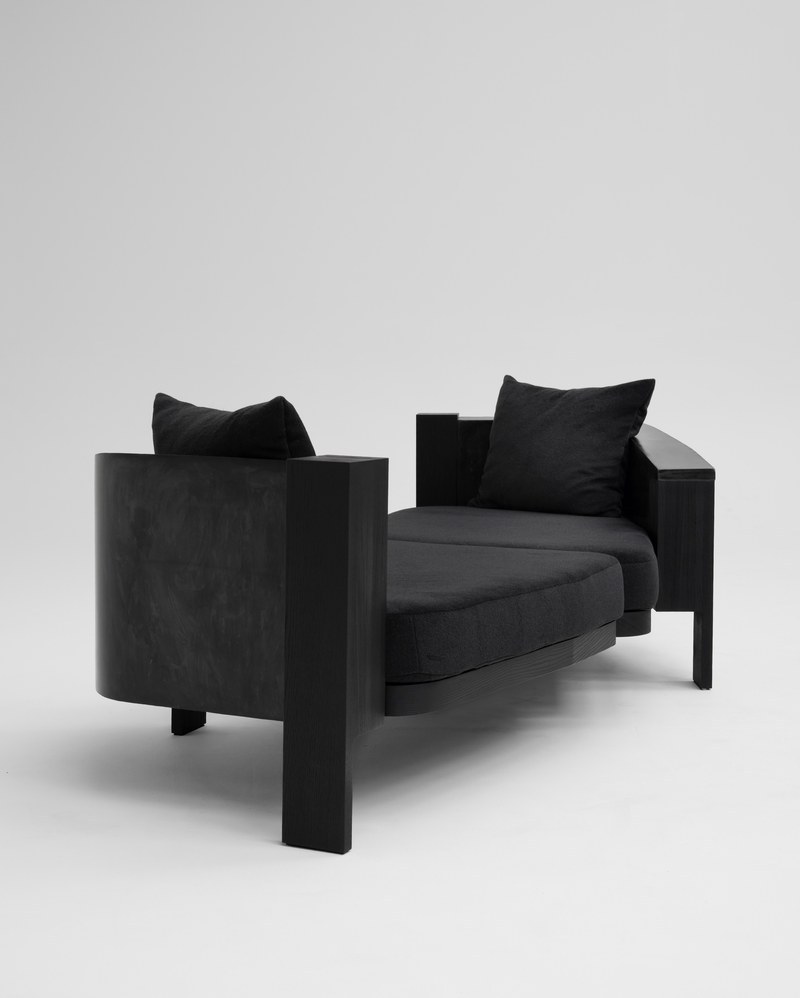 Custom asymmetrical black upholstered hotel lounge sofa with offset seats, curved exterior and substantial end supports