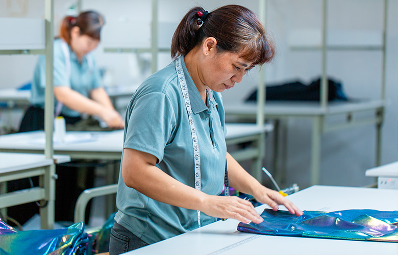 Staff measuring a sweatshirt sample and checking specifications, fabric swatches and technical documents for sample approval.