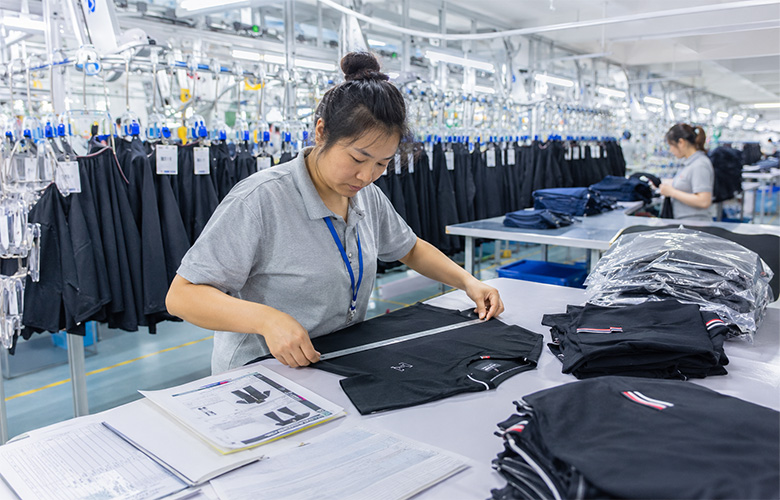 Quality control staff inspecting bulk garments in the factory by measuring finished apparel against approved specifications.