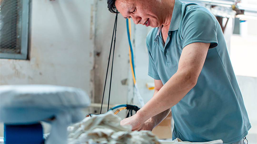Factory worker examining light-colored garment components beside production equipment