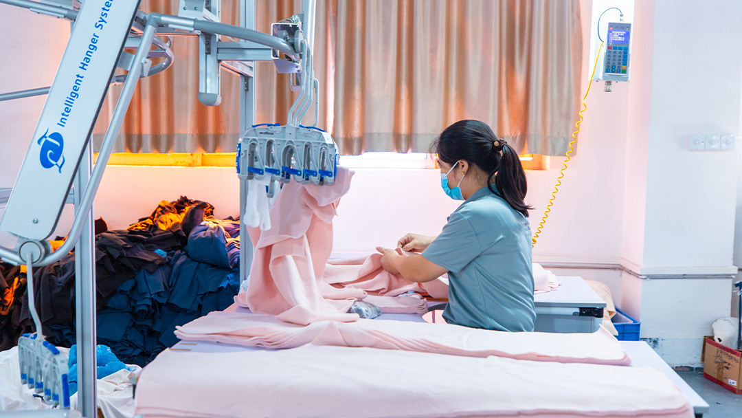 Garment worker handling pink fabric components beside an intelligent hanger system