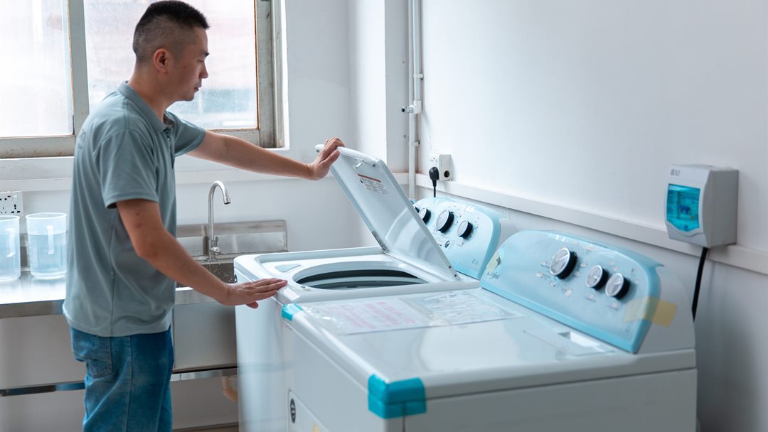 Technician operating washing equipment for garment material testing