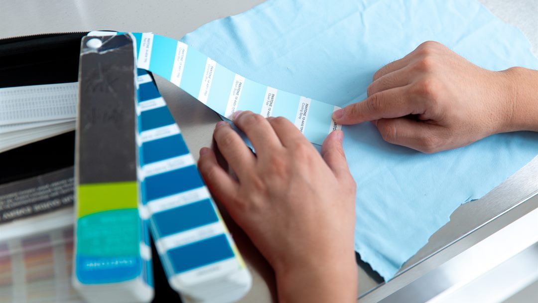 Hands comparing light blue fabric with blue colour reference cards during fabric selection for a hoodie project