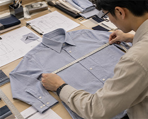 Person measuring a blue button-front shirt laid flat on a worktable